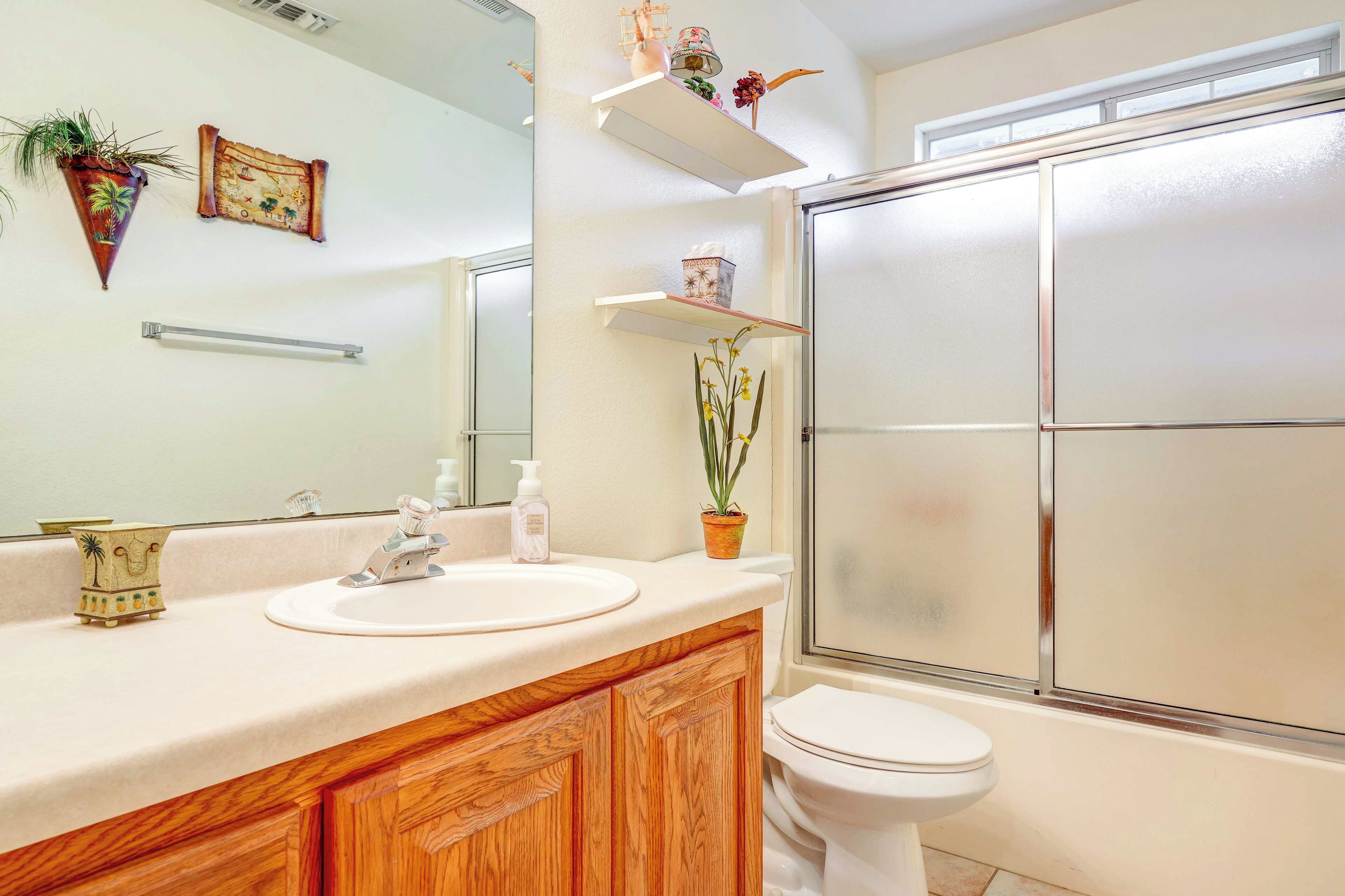 Un baño con tocador de madera, lavamanos blanco, espejo, inodoro y puerta de ducha con vidrio esmerilado.