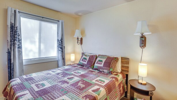 A bedroom with a large bed, two bedside lamps, a window with curtains, and a nightstand with a lamp. - 'grizzly Pine' Cottage - Walk to Ski Beach Park! (Big Bear Lake)