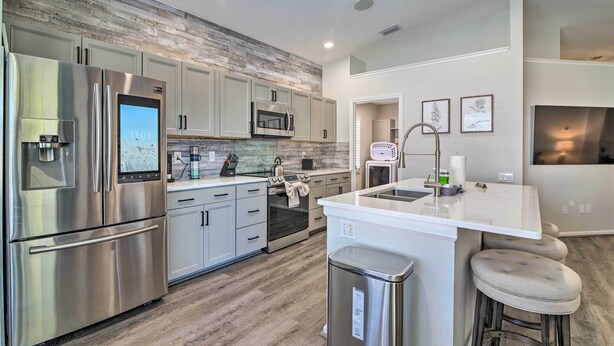 A modern kitchen with stainless steel appliances, a large island with stools, and a rustic wooden accent wall.