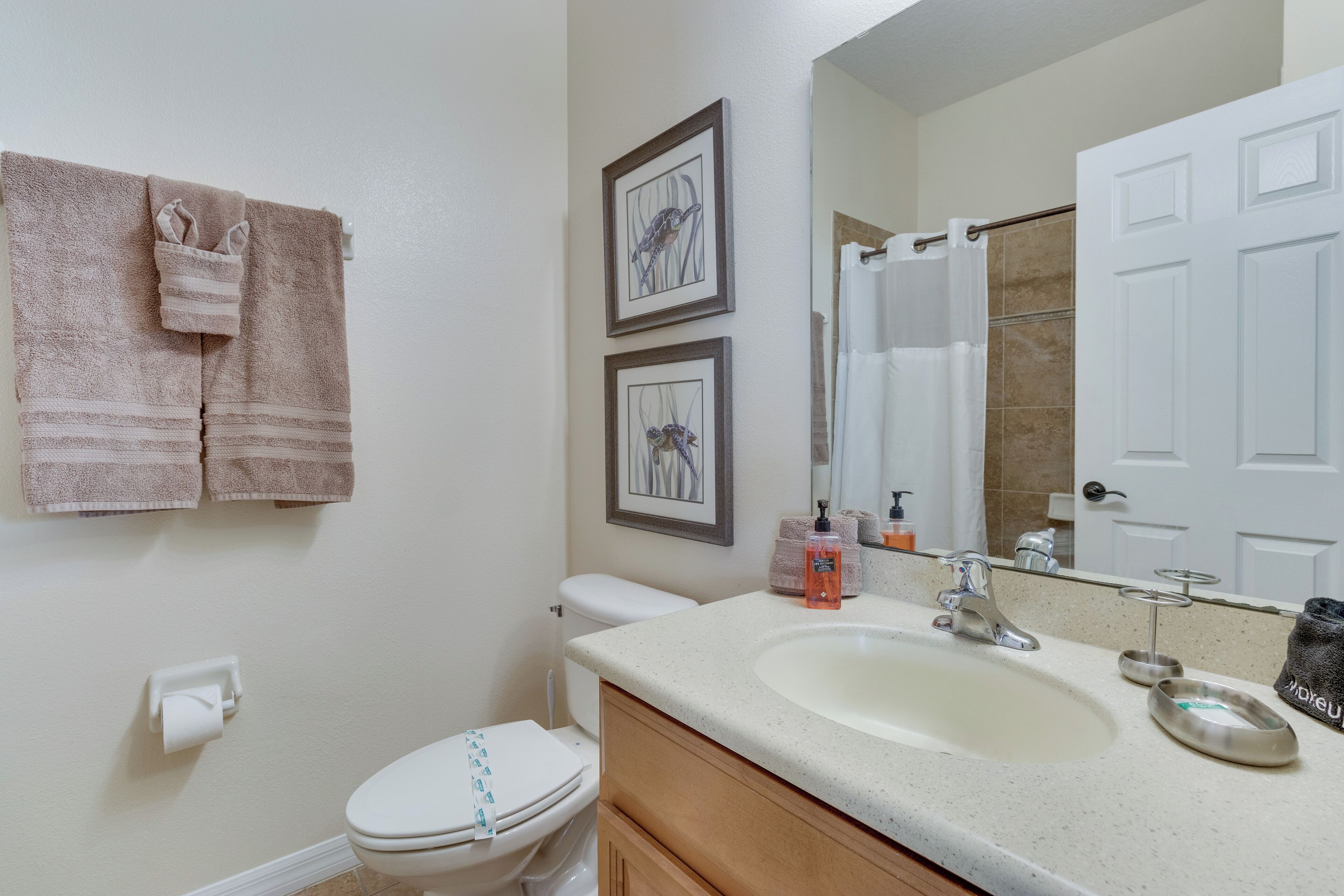 A bathroom with a toilet, sink, and two framed pictures on the wall.