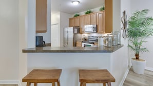 A kitchen with wooden cabinets, a microwave, a refrigerator, and a potted plant. - Kissimmee Retreat w/ Pool Access < 4 Mi to Disney! (Kissimmee)