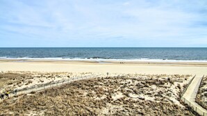 Una platja amb sorra, una passera de fusta i l'oceà al fons.