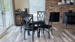A dining area with a brick wall, a ceiling fan, and a large window with blinds.