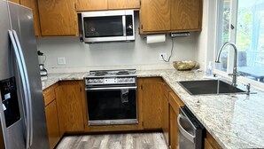 A modern kitchen with wooden cabinets, a stainless steel refrigerator, a microwave, a stove, and a sink.
