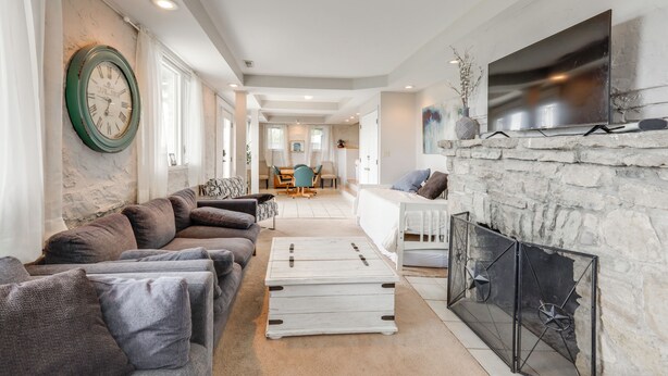 A modern living room with a stone fireplace, a large flat-screen TV, and a cozy seating area with a sectional sofa and ottoman. - Riverview Hideaway, 3 Mi to Dtwn Cincinnati (Cincinnati)