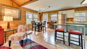 A cozy cabin interior with a wooden dining area, a kitchen with a stainless steel refrigerator, and a large window providing a view of the outdoors. - High Peak Heaven: Cozy Log Cabin on 1 Acre! (Hensonville)