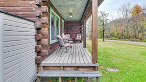 A wooden cabin with a porch, a fireplace, and a view of the surrounding forest. - High Peak Heaven: Cozy Log Cabin on 1 Acre! (Hensonville)