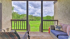 A covered porch with a view of a green field, a wicker chair, a blue sofa with pillows, and a railing.