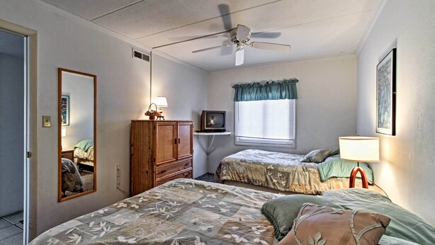 Un dormitorio con dos camas, ventilador de techo, televisor y ventana con cortinas.