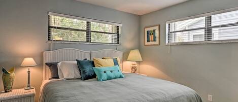 A bedroom with a bed, two bedside tables, two lamps, and two windows with blinds.