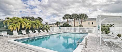 A rectangular swimming pool with a white deck, surrounded by lounge chairs and palm trees.