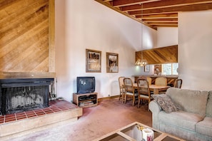 A living room with a fireplace, a television, a dining area with chairs, and two framed pictures on the wall.