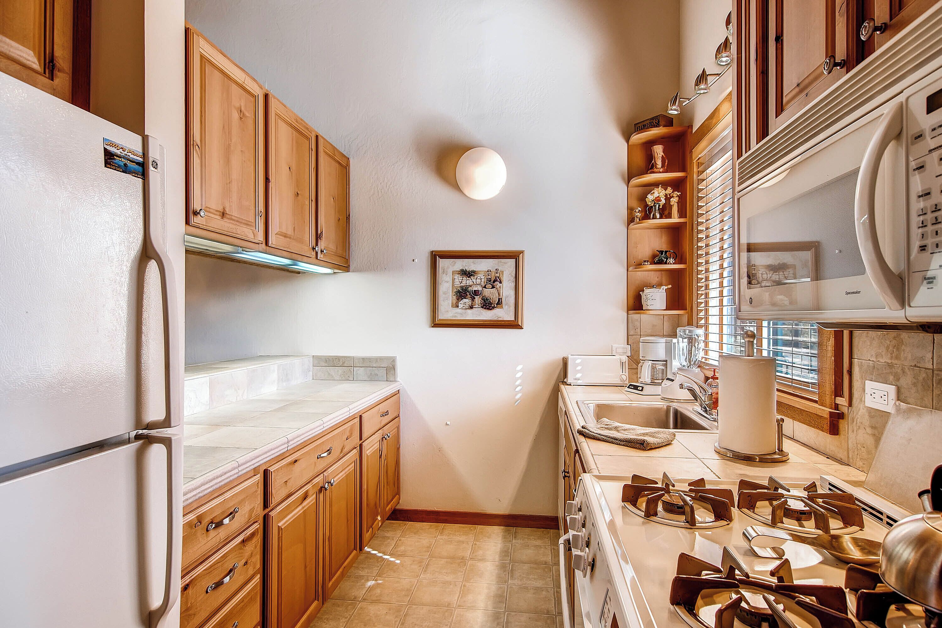 A kitchen with wooden cabinets, a refrigerator, a stove, and a sink.