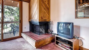 A living room with a fireplace, a television, and a sliding glass door leading to an outdoor area with chairs. - Inviting Ski Getaway < 1 Mile to Northstar Resort! (Truckee)