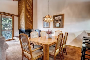 A dining area with a wooden table, wicker chairs, a hanging light fixture, and framed pictures on the wall.