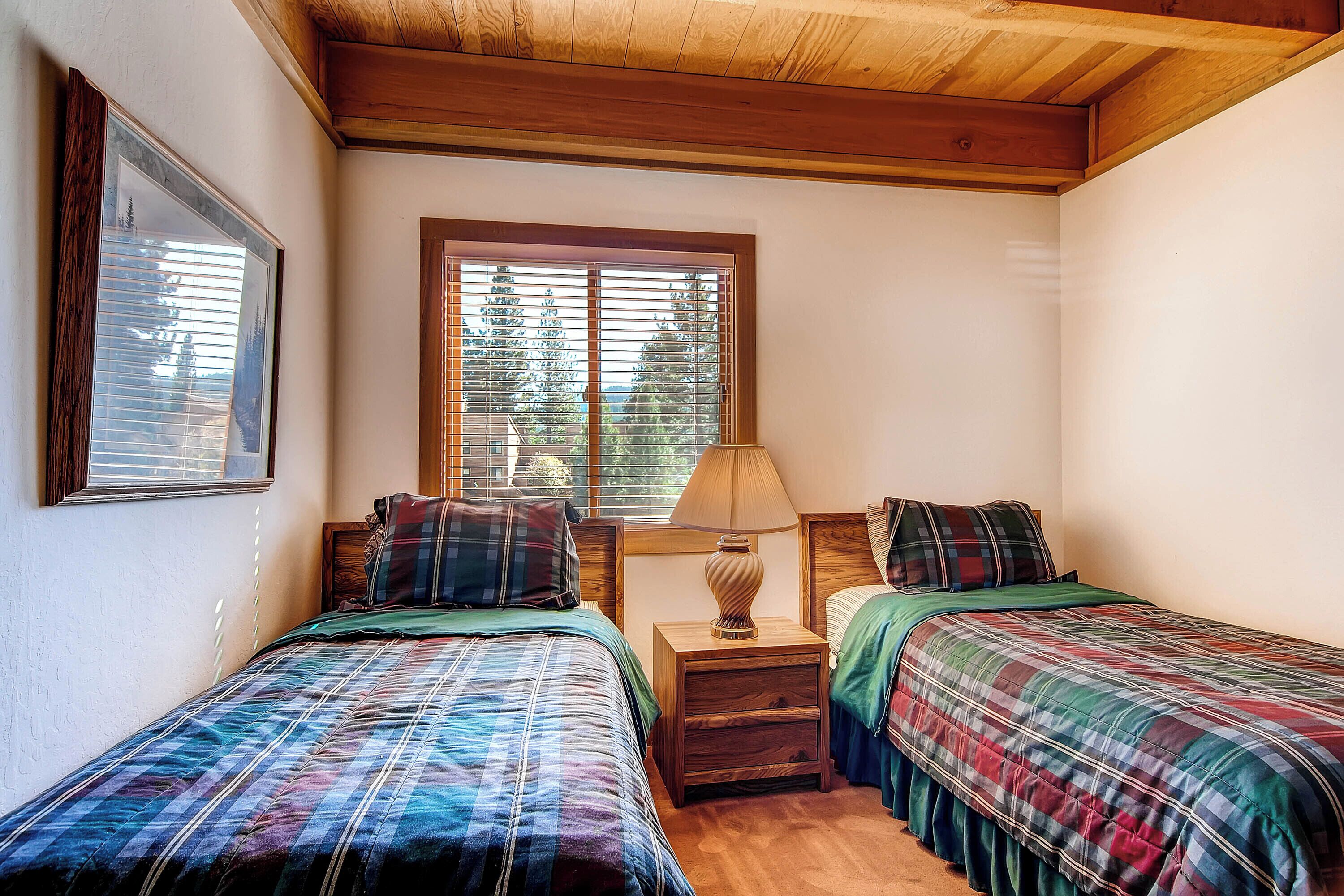 A bedroom with two beds, a nightstand with a lamp, and a window with blinds.