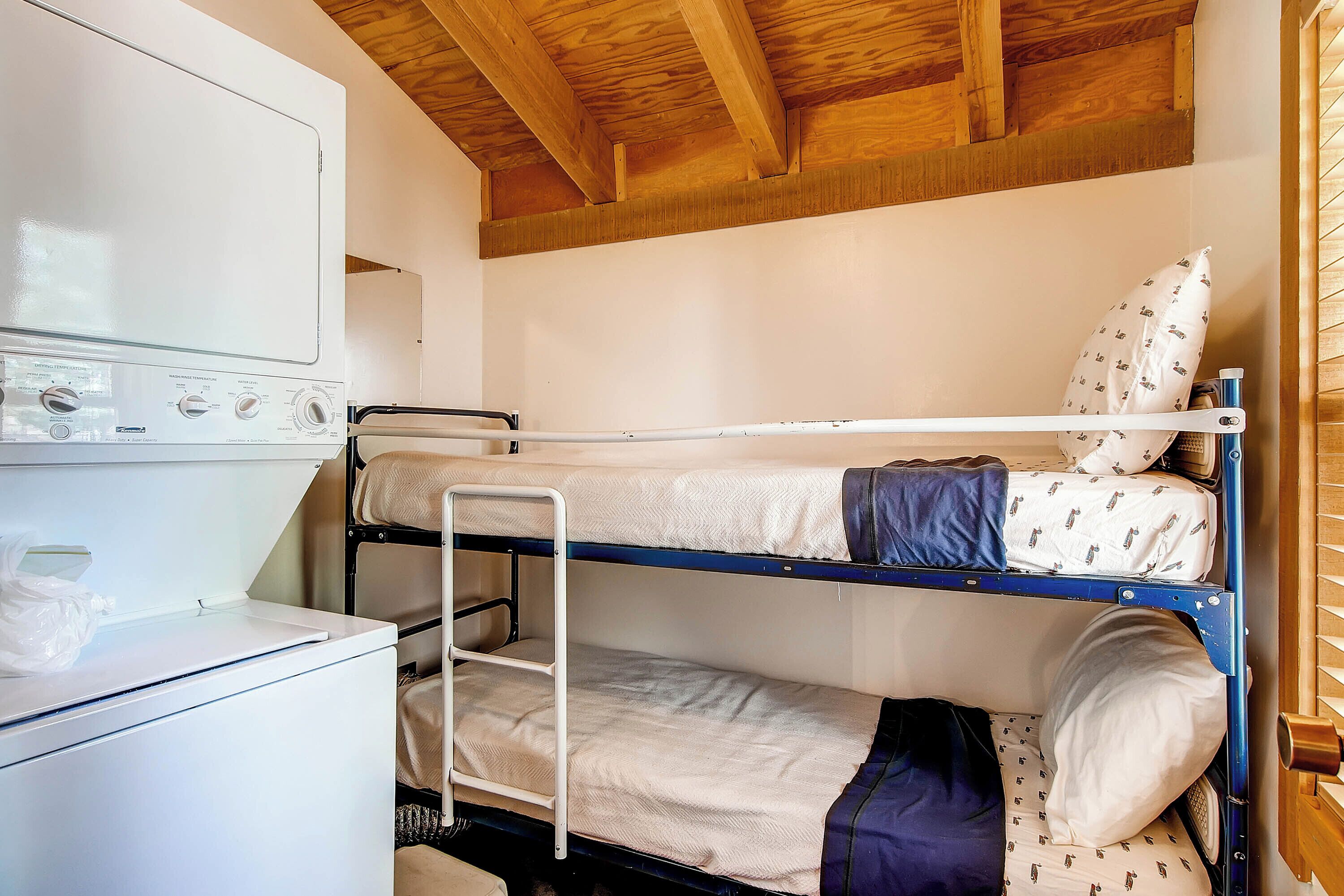 Een stapelbed met een ladder, een witte wasmachine en een houten plafond.