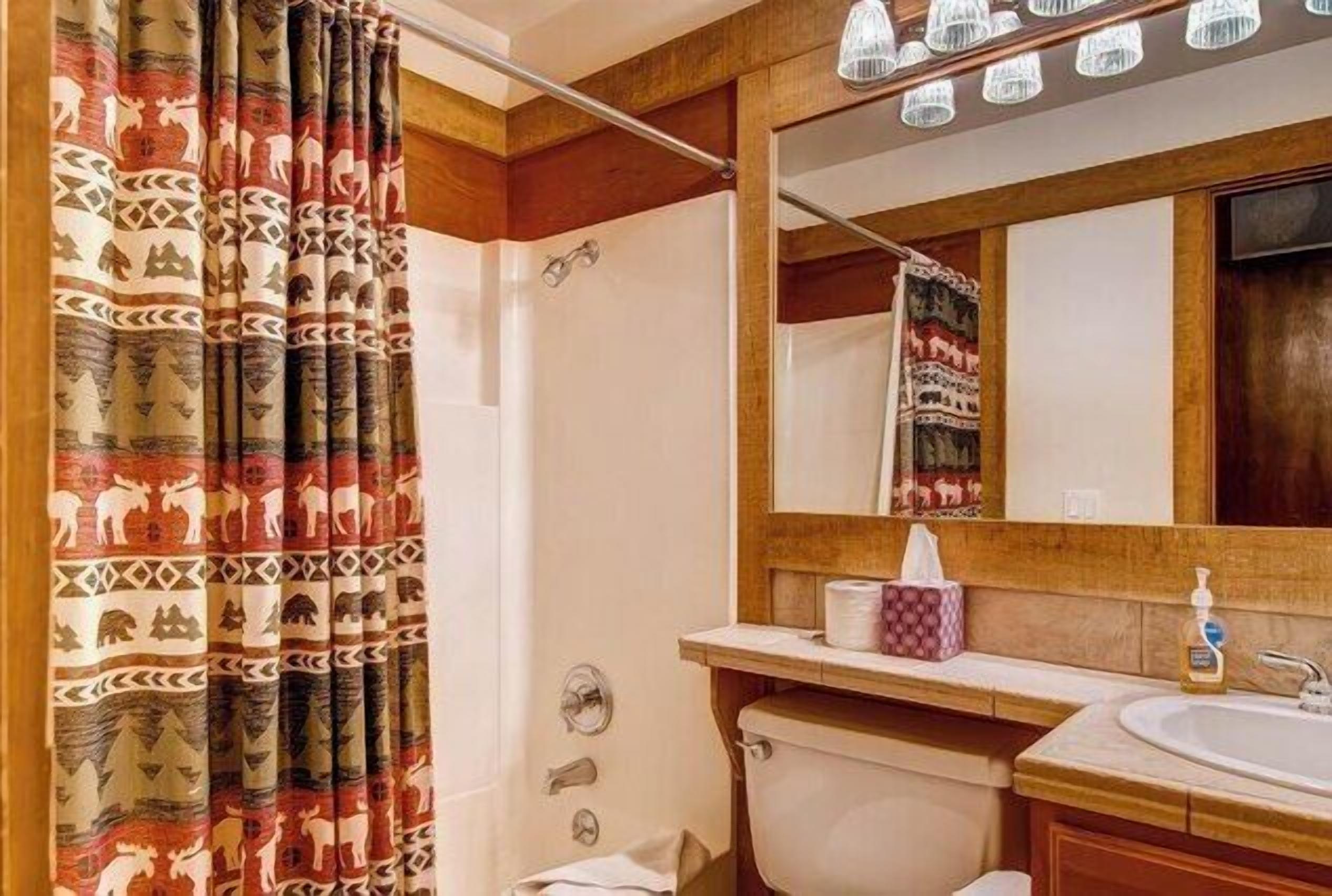 Une salle de bain avec un rideau de douche orné de motifs animaliers, un meuble-lavabo en bois avec un miroir et des toilettes.