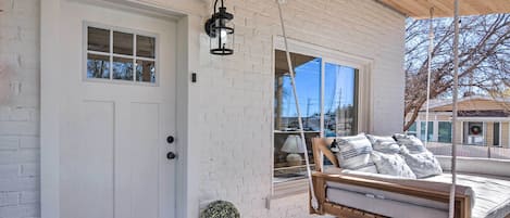 A white brick house with a front porch, a swing bed, a potted plant, and a hanging lantern.