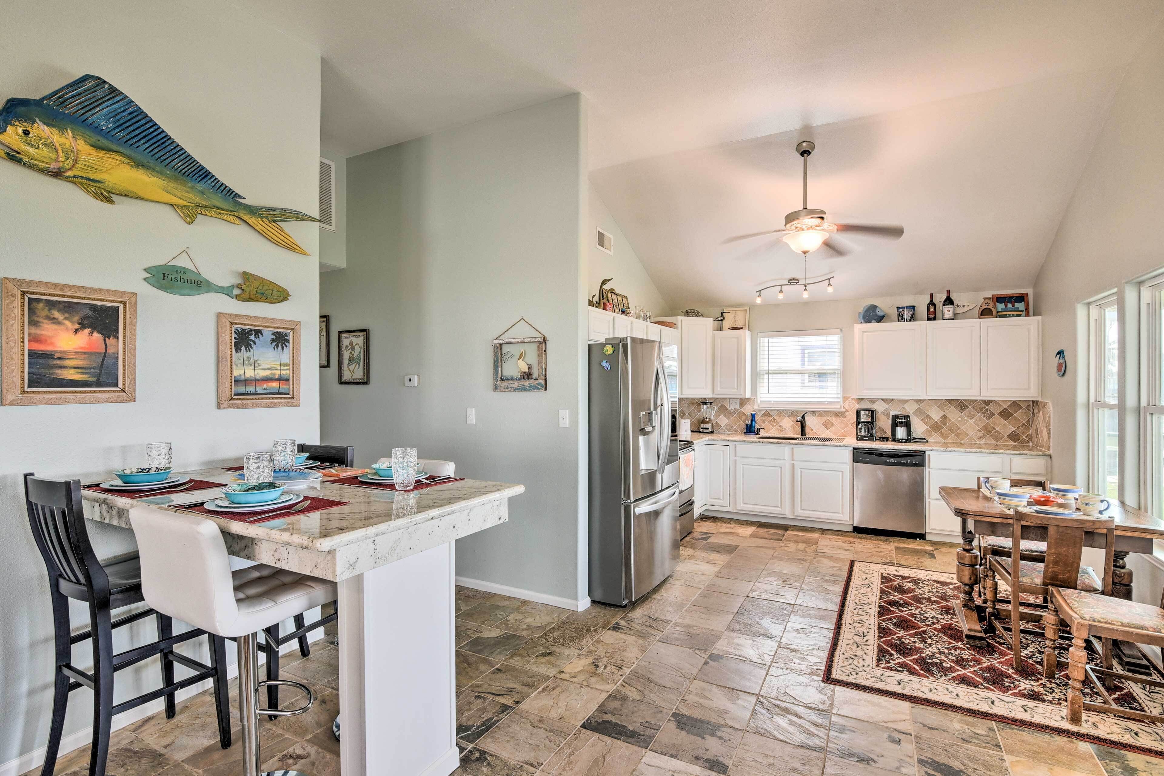A modern kitchen with white cabinets, a stainless steel refrigerator, and a dining area with a marble countertop and chairs.