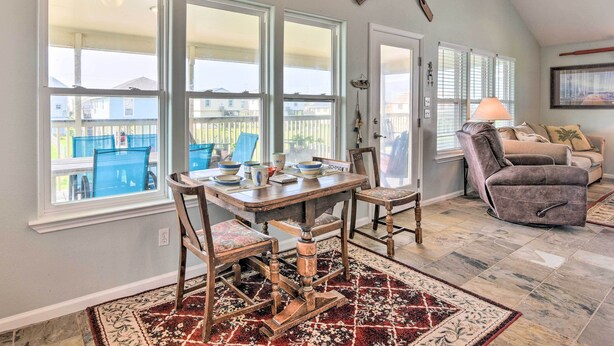 A dining area with a wooden table and chairs, a patterned rug, and large windows with a view of a fenced yard. - Unwind Poolside, Walk to Beach! Galveston Retreat (Galveston)