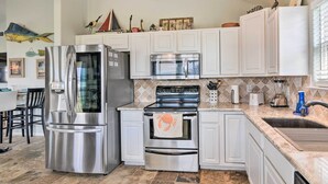 A kitchen with white cabinets, stainless steel appliances, a tiled backsplash, and a dining area with chairs. - Unwind Poolside, Walk to Beach! Galveston Retreat (Galveston)