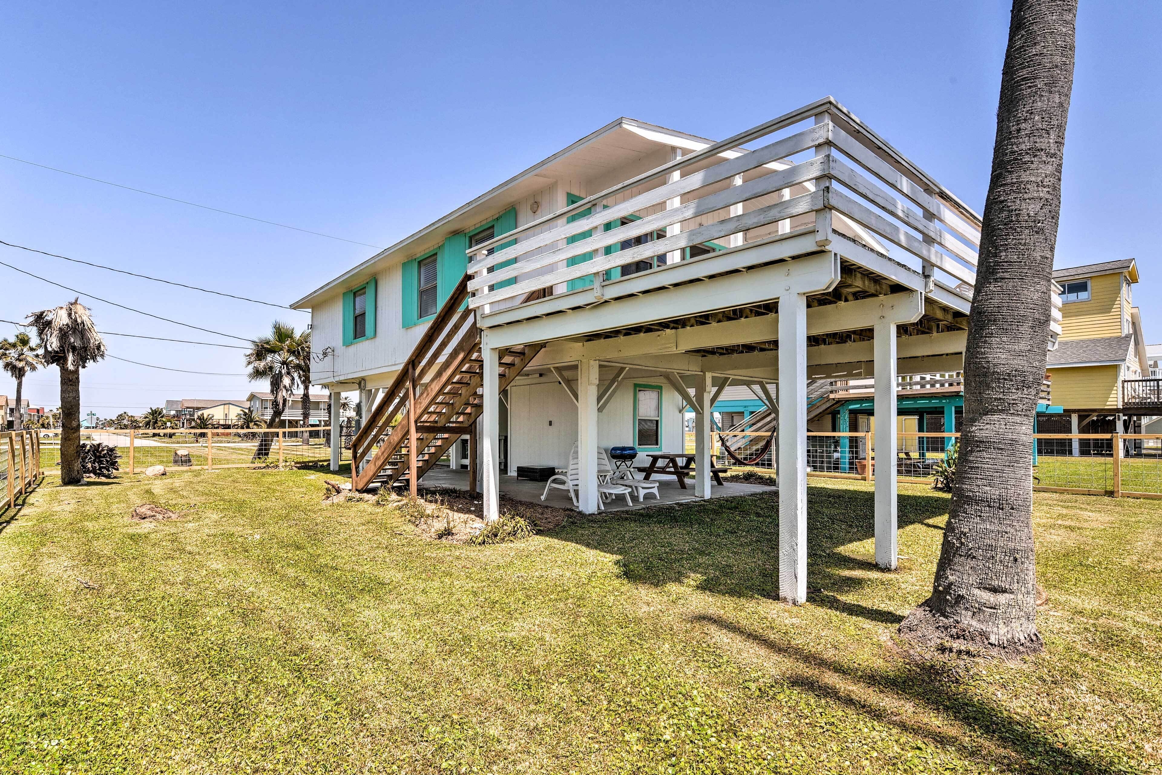 A beachfront house with a covered porch, outdoor seating, and a staircase leading to the upper level.