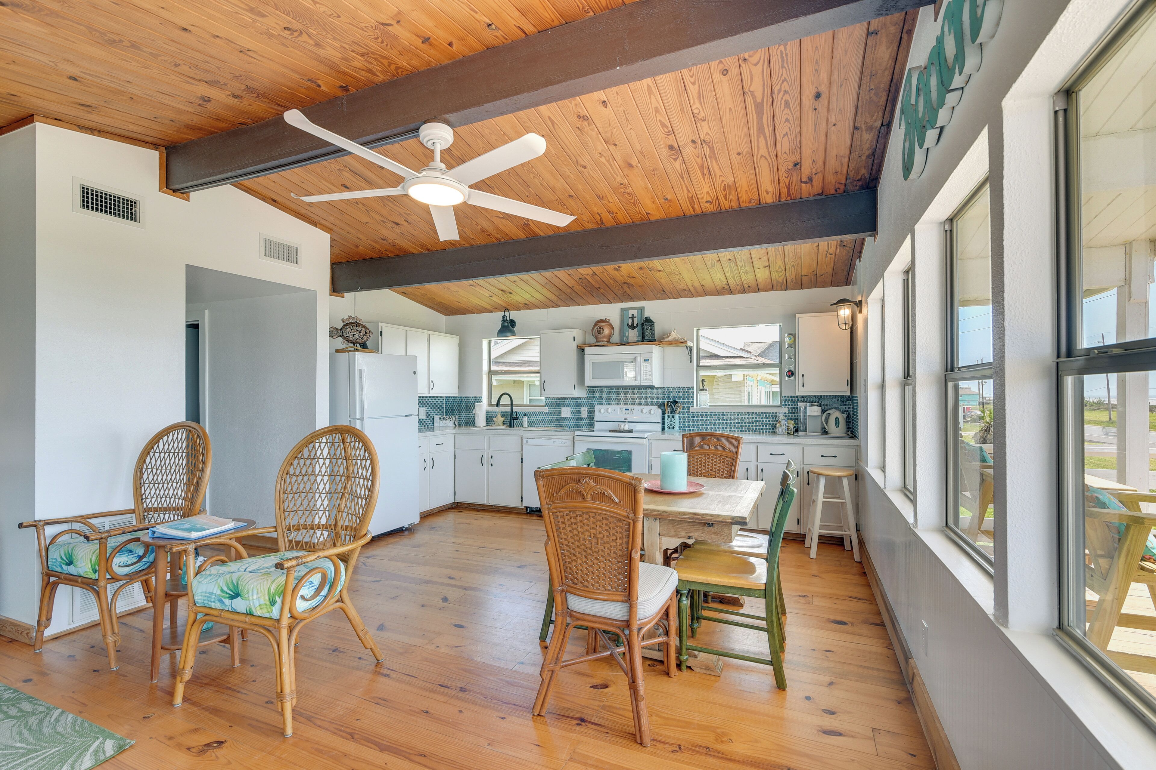 A spacious kitchen with wooden floors, white cabinets, and a dining area with wicker chairs and a table.