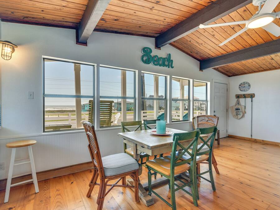 A dining area with a wooden ceiling, large windows, and a table with chairs.