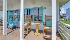 A covered porch with wooden chairs and a table, white walls with teal trim, and large windows. - Gulf Coast Views: Stilted Retreat in Galveston! (Galveston)