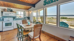 A kitchen with wooden cabinets, a white stove, and a dining area with wicker chairs and a table. - Gulf Coast Views: Stilted Retreat in Galveston! (Galveston)