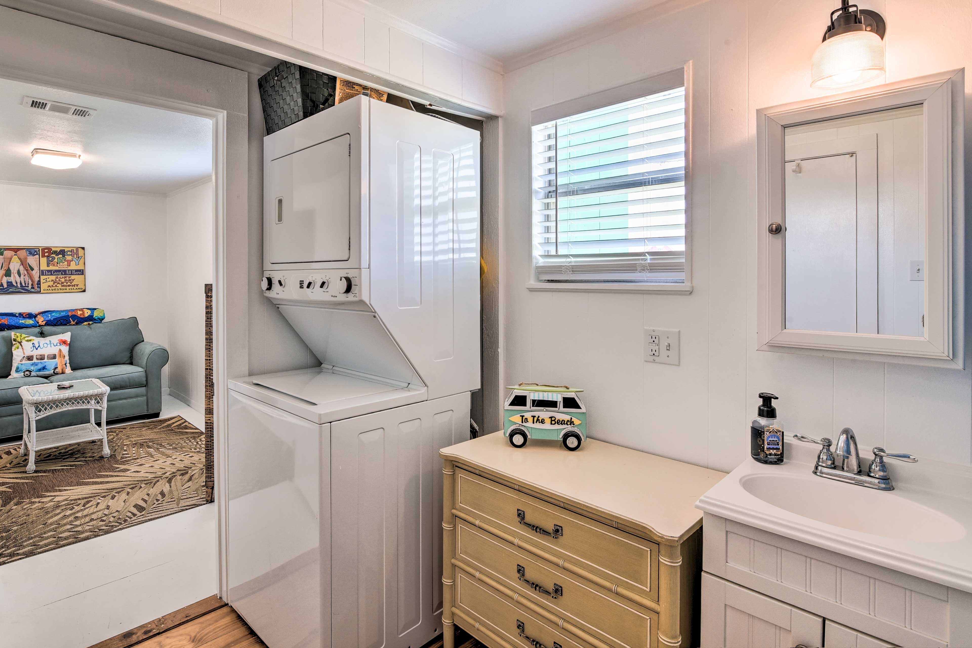 A compact, modern bathroom with a built-in washer and dryer, a small vanity with a mirror, and a beach-themed toy on the counter.