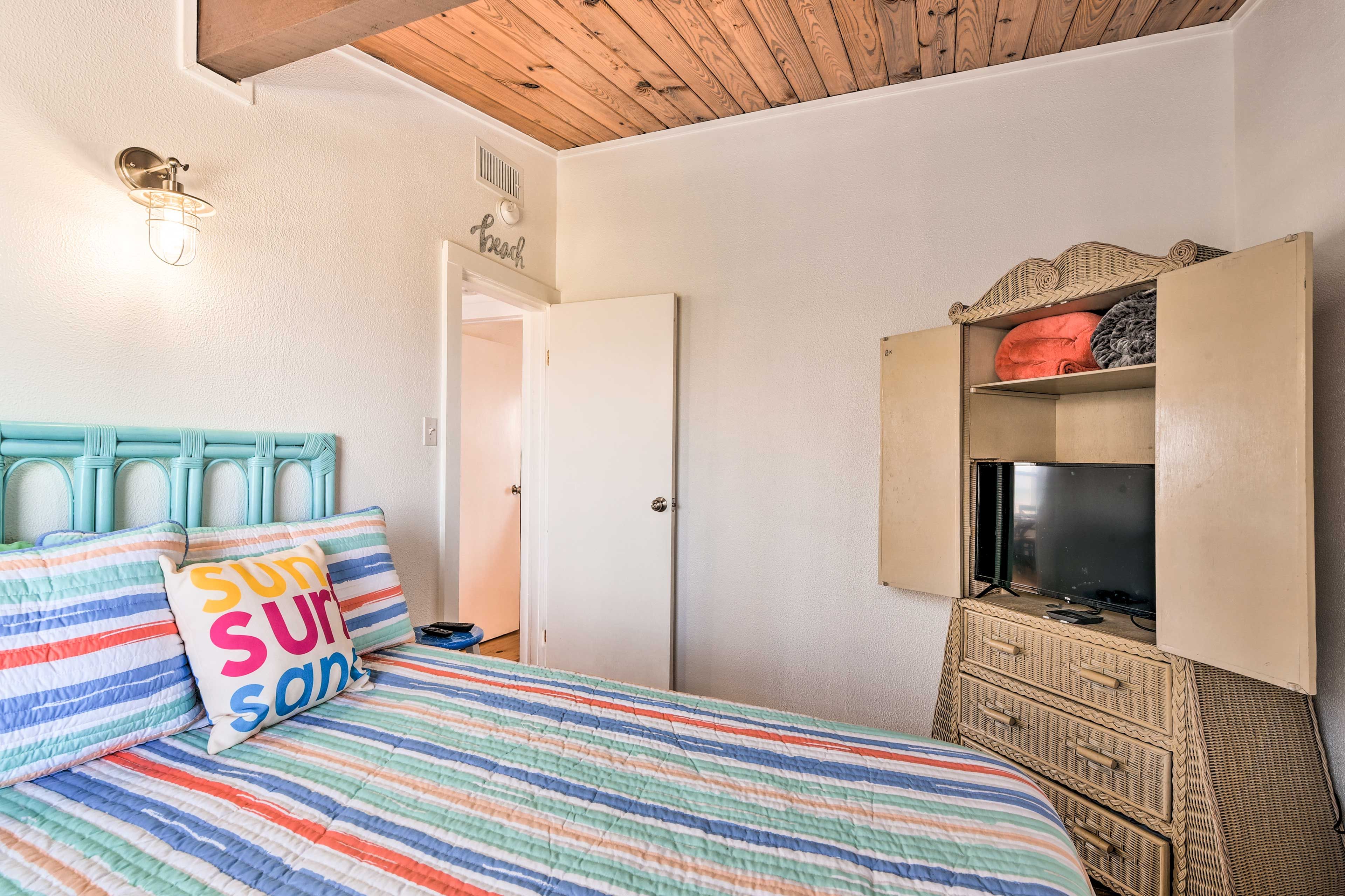 Un dormitorio con edredón a rayas, cabecera color turquesa, televisor sobre un mueble y una puerta con la etiqueta 'Beach'.
