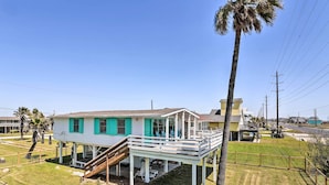 A two-story house with a balcony, a staircase leading to the upper floor, and a fenced yard with palm trees. - Gulf Coast Views: Stilted Retreat in Galveston! (Galveston)