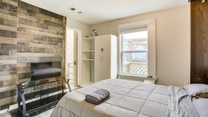 A bedroom with a wooden wall, a bed with a blanket, a TV on a stand, and a window with a view.