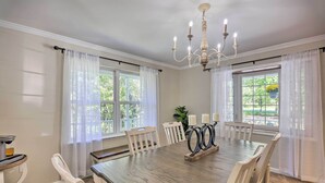 A dining room with a large wooden table, white chairs, a chandelier, and large windows with sheer curtains. - Poconos Escape w/ Hot Tub & Fire Pit (Albrightsville)