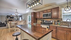 A modern kitchen with wooden cabinets, a central island, a stone backsplash, and a built-in microwave. - Poconos Escape w/ Hot Tub & Fire Pit (Albrightsville)