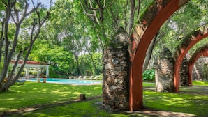 Un jardin luxuriant agrémenté d’une arche en pierre, d’une piscine et d’un belvédère.