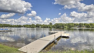 A wooden dock extending into calm water, surrounded by lush greenery and a clear sky.