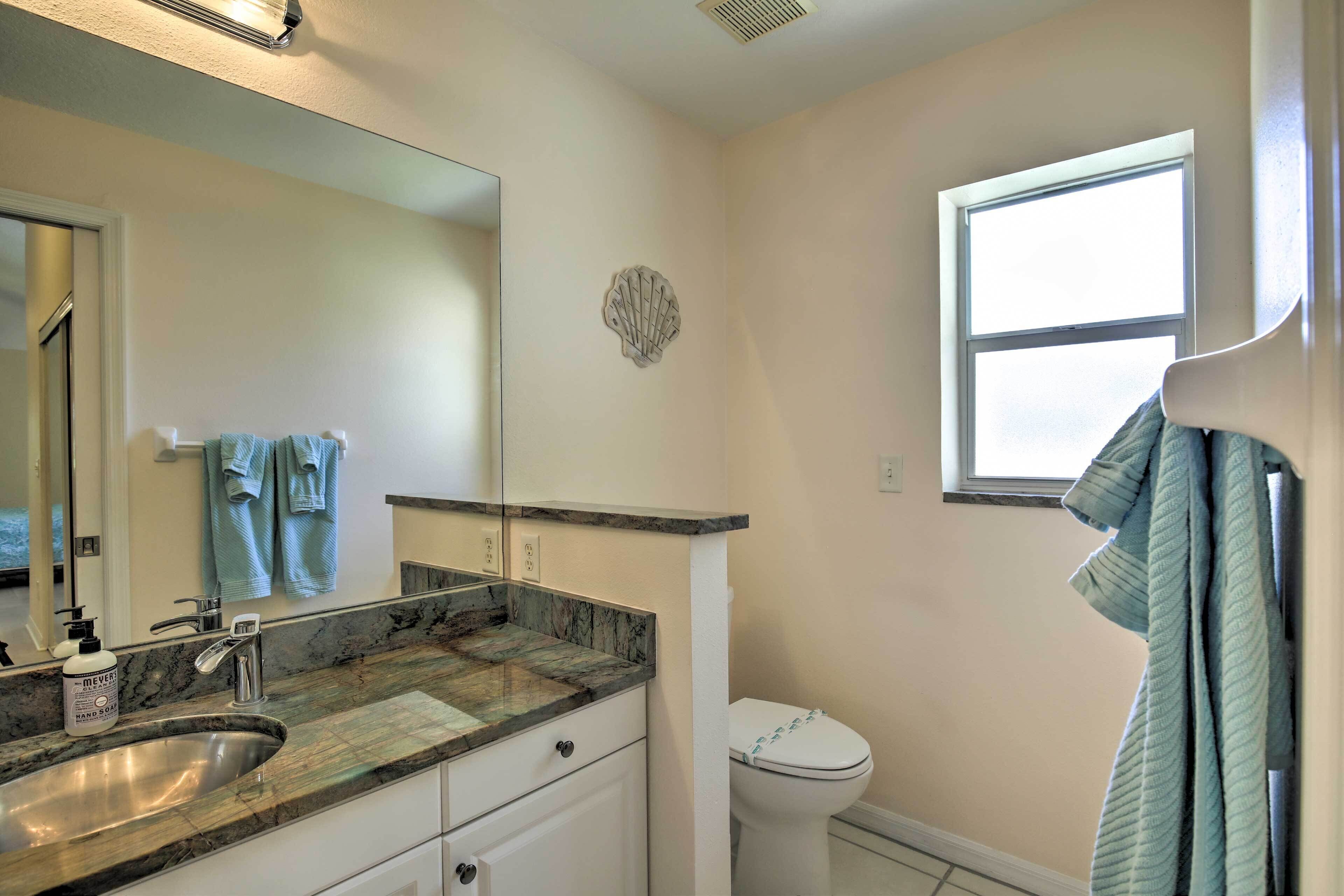 A bathroom with a sink, mirror, towel rack, toilet, and a window.