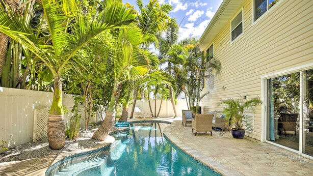 A swimming pool with a curved design, surrounded by palm trees and potted plants. - Indian Rocks Beach Oasis - 2 Blocks to Beach! (Indian Rocks Beach)