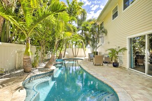 A swimming pool with a curved design, surrounded by palm trees and potted plants. - Indian Rocks Beach Oasis - 2 Blocks to Beach! (Indian Rocks Beach)