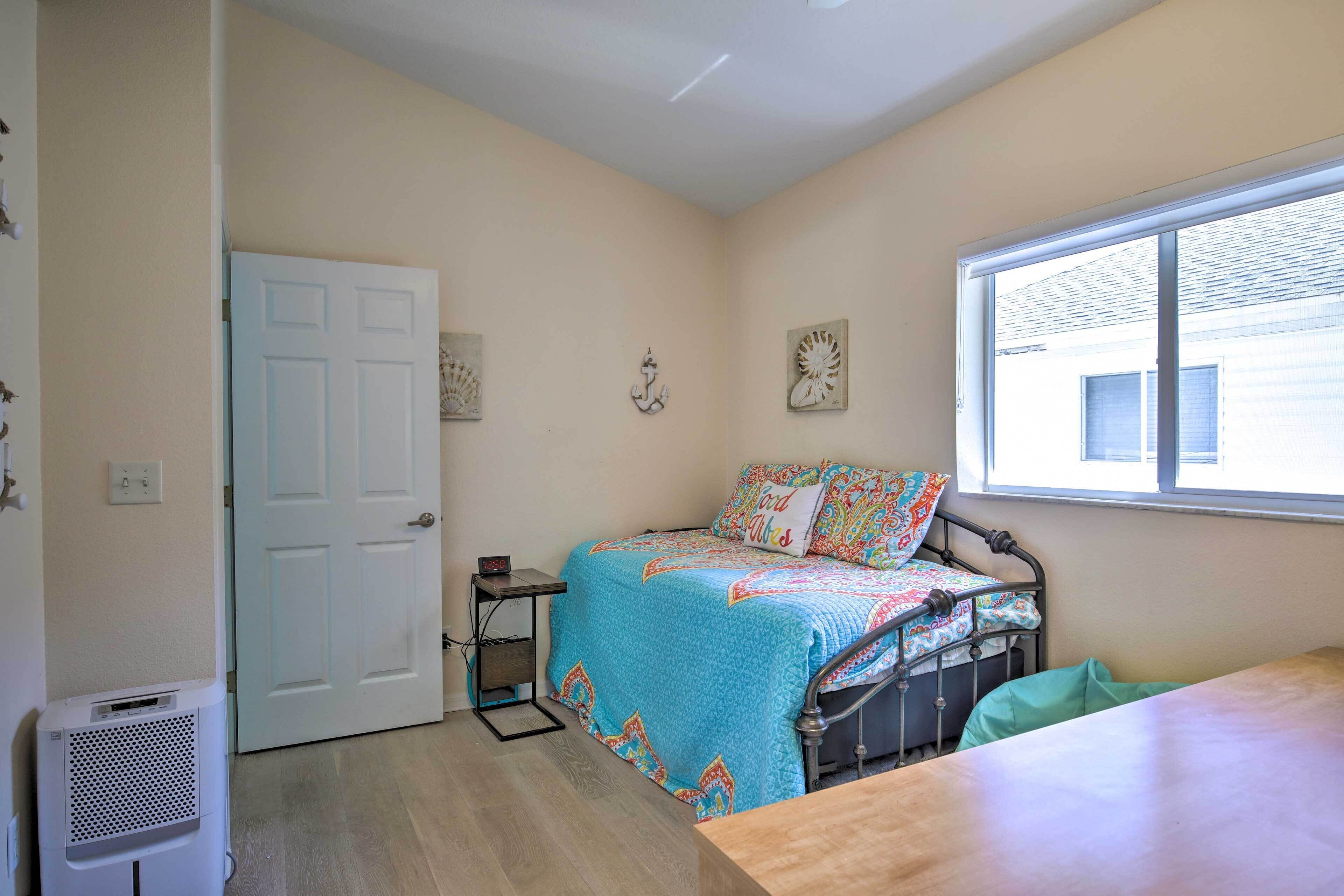 Un dormitorio con una cama, una ventana, una puerta y una mesita.