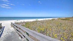 A beach with a wooden boardwalk leading to the shore, sandy beach, and clear blue sky. - Indian Rocks Beach Oasis - 2 Blocks to Beach! (Indian Rocks Beach)
