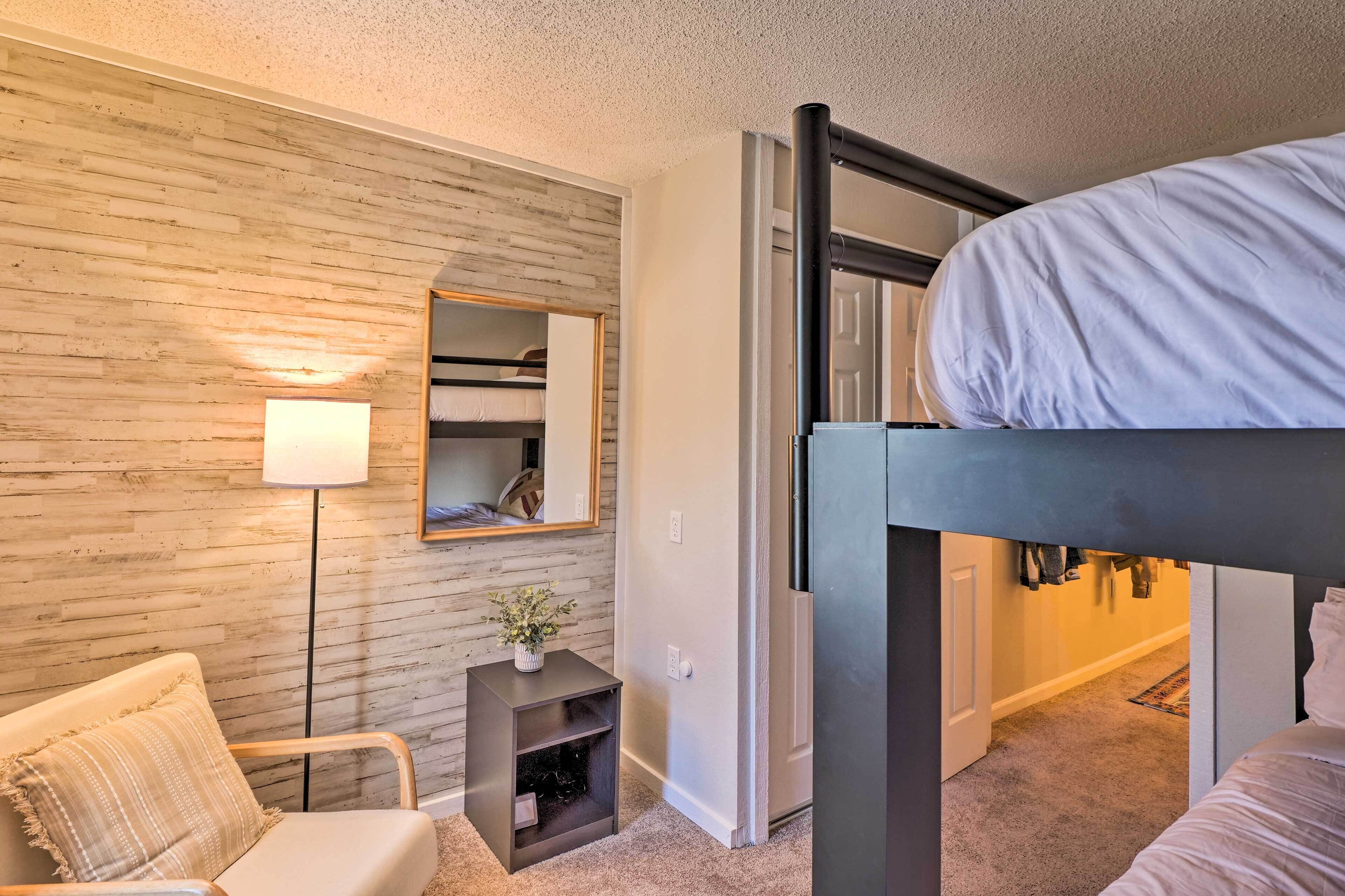 Un dormitorio con una cama nido, una mesita de noche con lámpara, una silla y un espejo en la pared.
