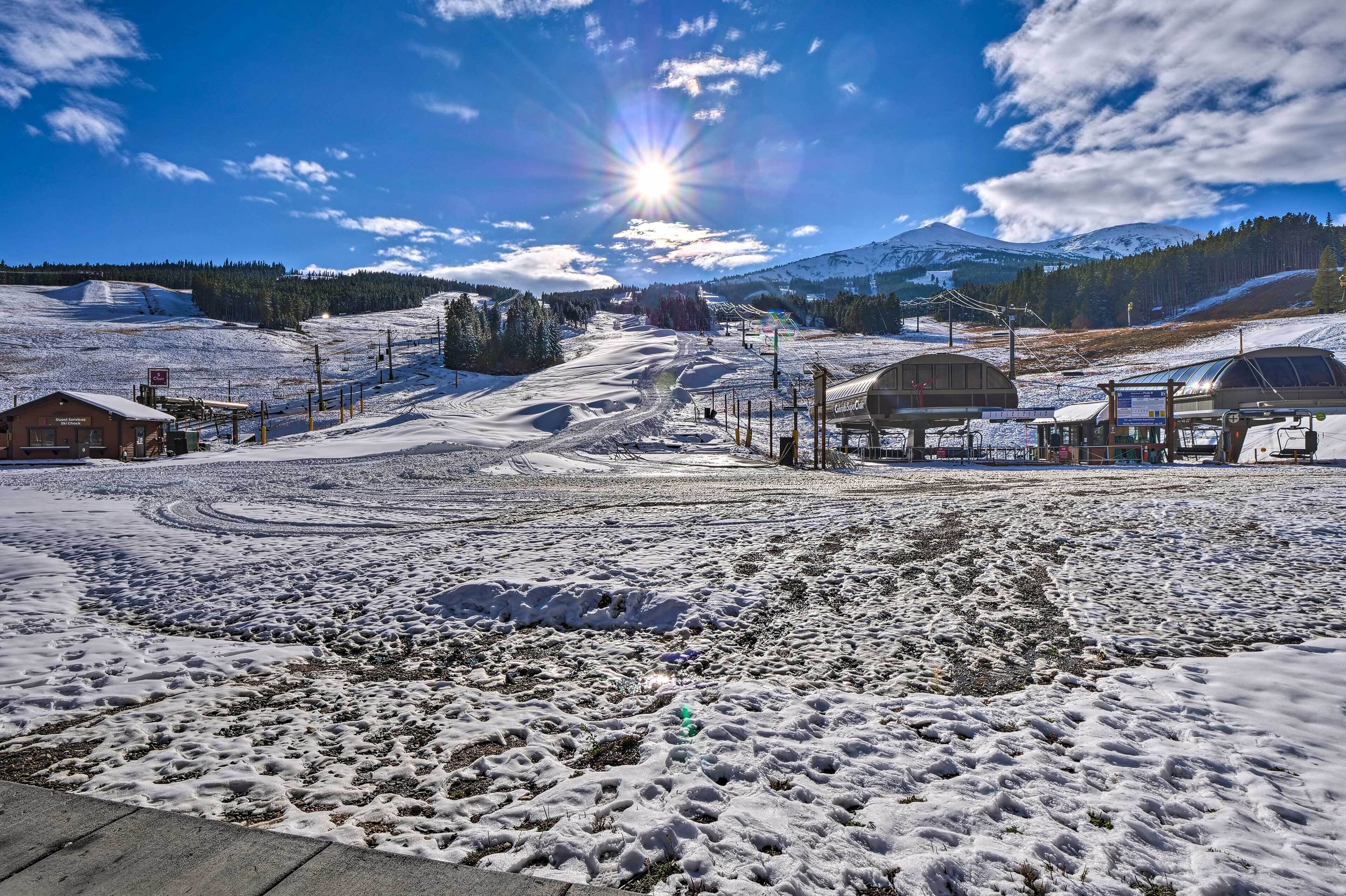 A snow-covered ski resort with a clear sky, a sun shining, and a mountain in the background.