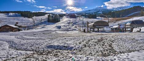 A snow-covered ski resort with a clear sky, a sun shining, and a mountain in the background.