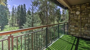 A balcony with a stone wall, a metal railing, and a view of a forest. - Walk to Main St & Ski Lift: Breck Condo w/ Pool! (Breckenridge)