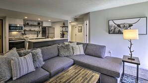 A modern living room with a grey sectional sofa, a coffee table, and a kitchen area with built-in appliances. - Walk to Main St & Ski Lift: Breck Condo w/ Pool! (Breckenridge)