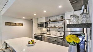 A modern kitchen with a white marble countertop, stainless steel appliances, and a vase with yellow flowers. - Walk to Main St & Ski Lift: Breck Condo w/ Pool! (Breckenridge)